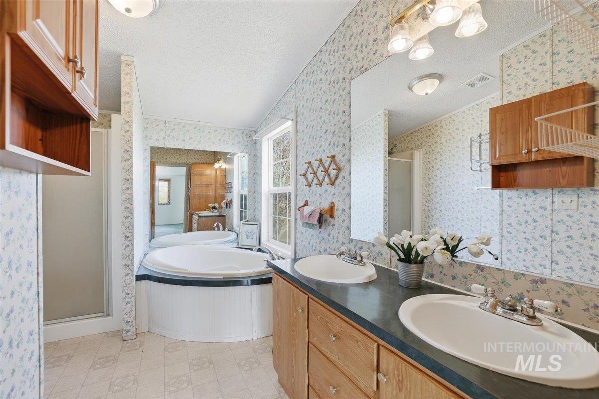 Bathroom with a shower stall, a textured ceiling, a garden tub, double vanity, and wallpapered walls