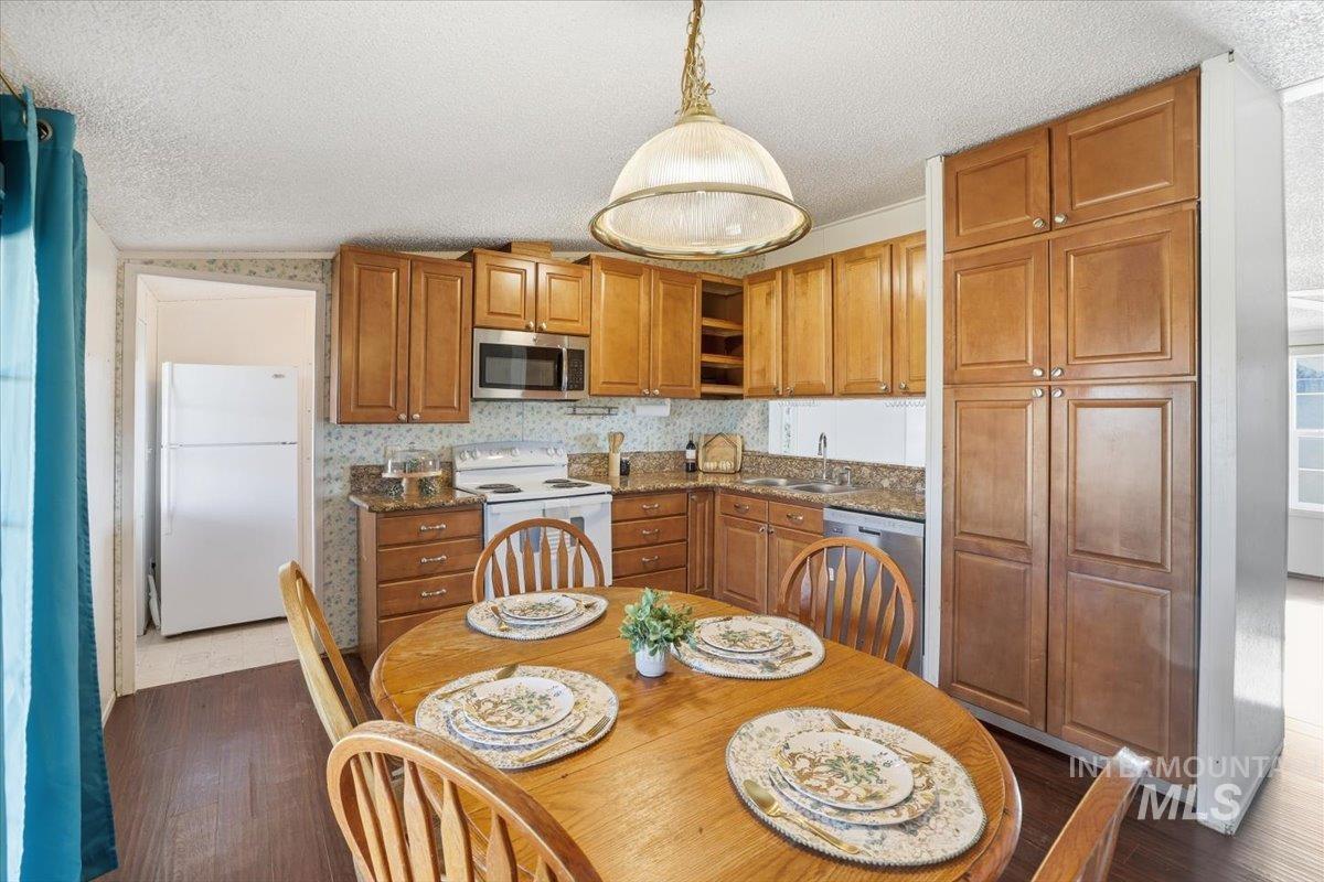 Kitchen featuring appliances with stainless steel finishes, brown cabinets, hanging light fixtures, a textured ceiling, and dark stone counters