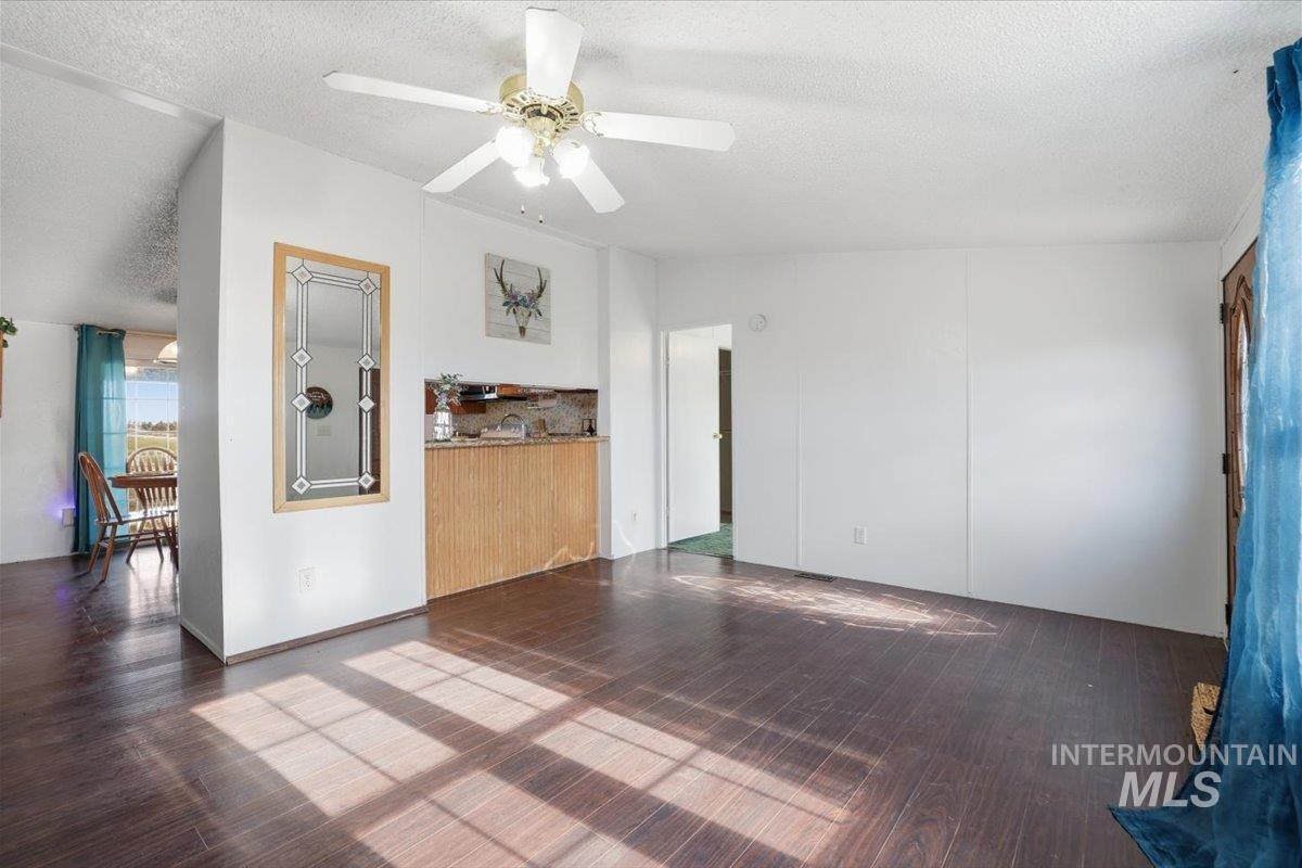 Unfurnished living room featuring a textured ceiling, dark wood-style flooring, ceiling fan, and lofted ceiling