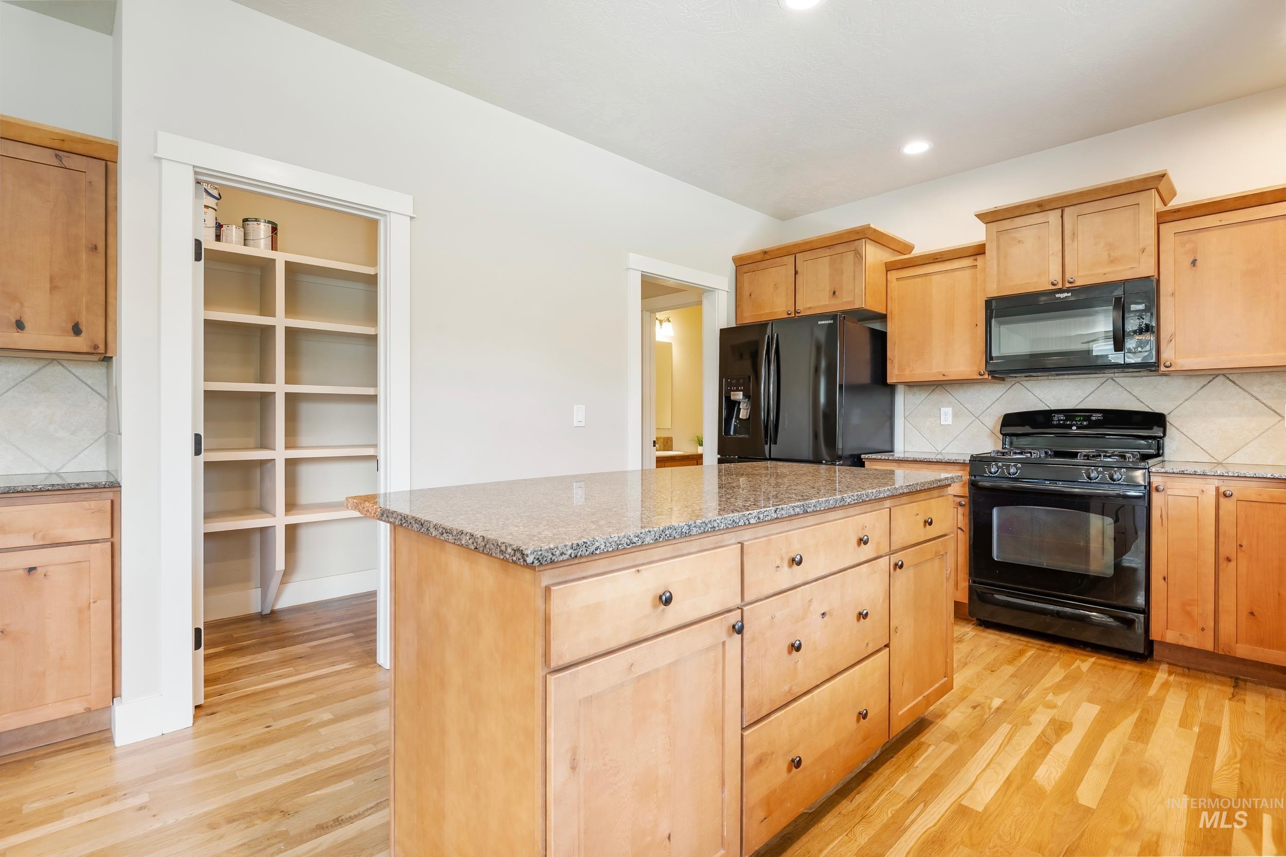 Kitchen featuring backsplash, black appliances, light brown cabinets, a kitchen island, and light wood-style flooring