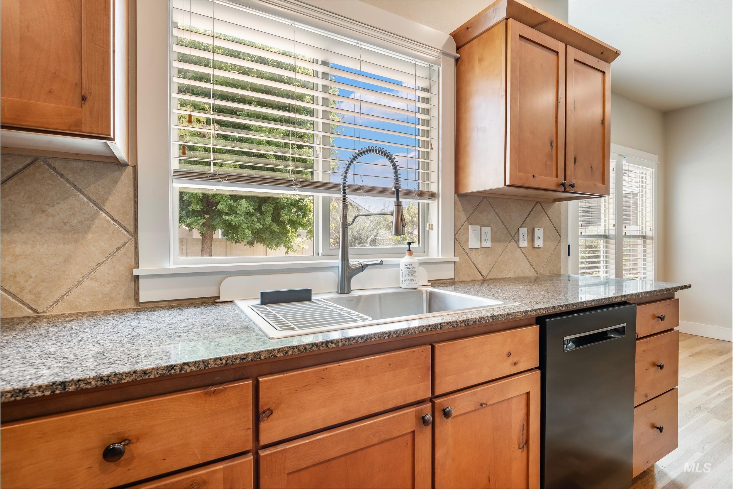 Kitchen featuring backsplash, light stone countertops, dishwasher, light wood-type flooring, and brown cabinets