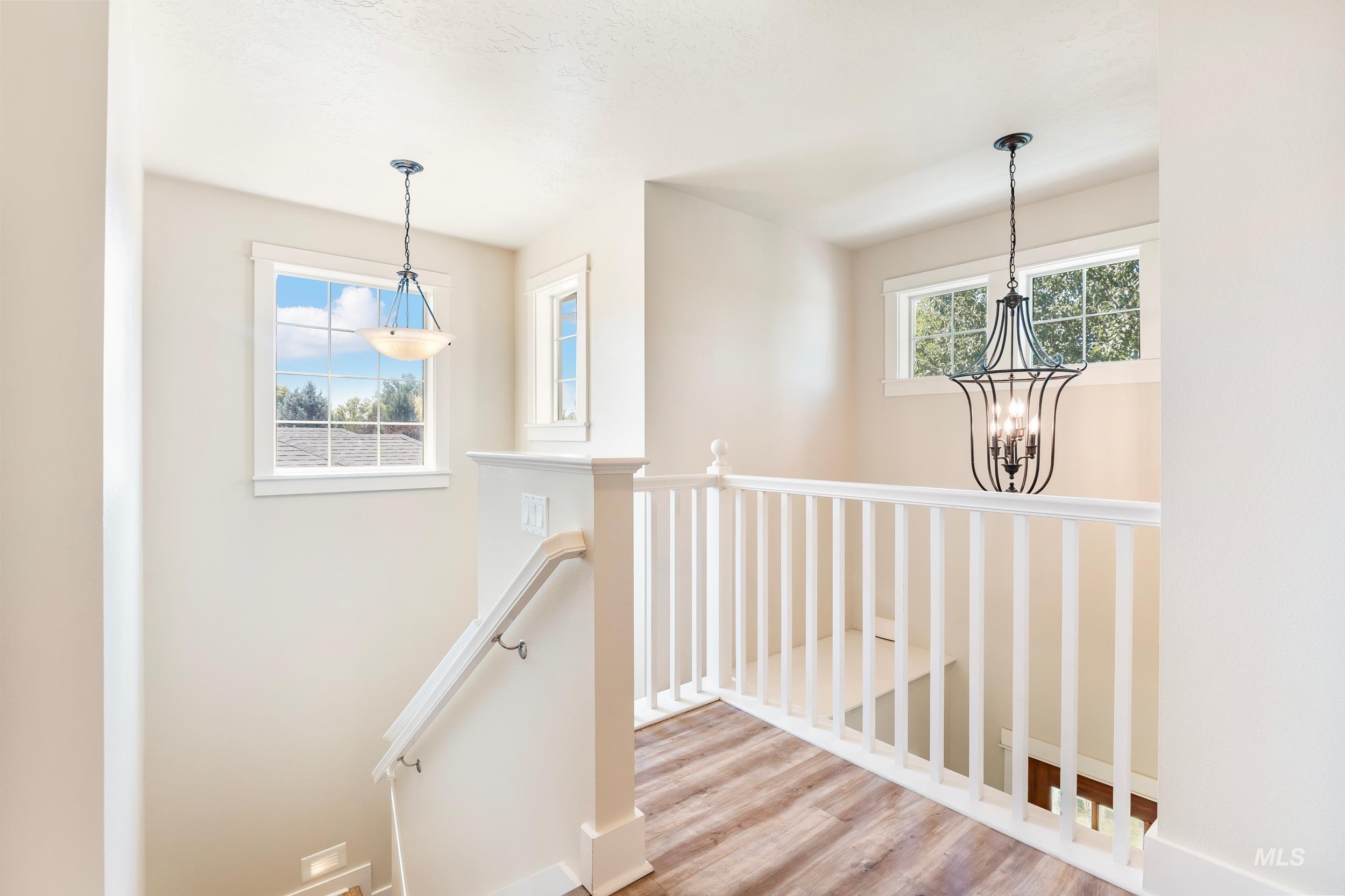 Corridor with an upstairs landing, wood finished floors, plenty of natural light, and a chandelier