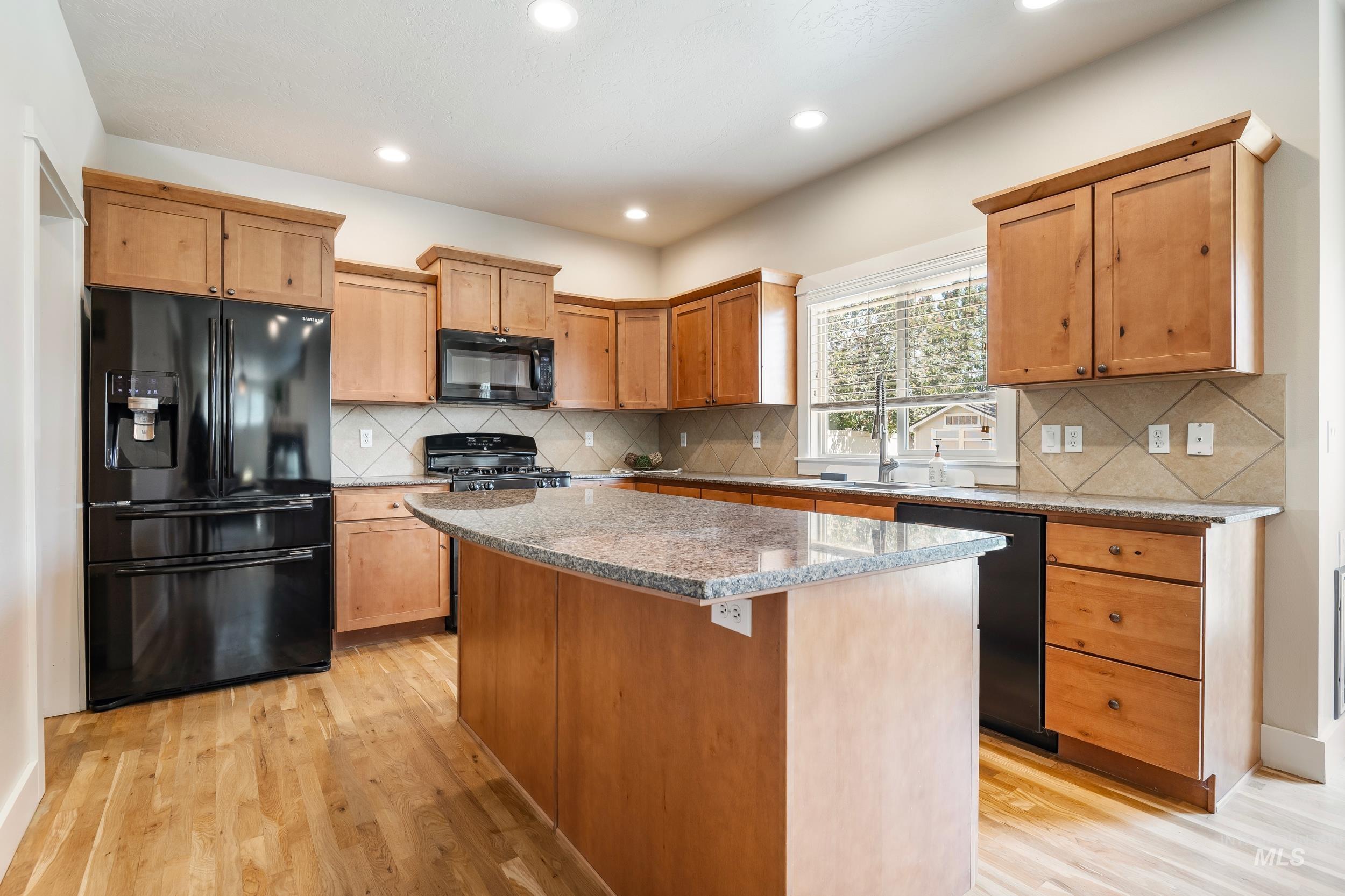 Kitchen with black appliances, tasteful backsplash, light stone counters, recessed lighting, and a center island