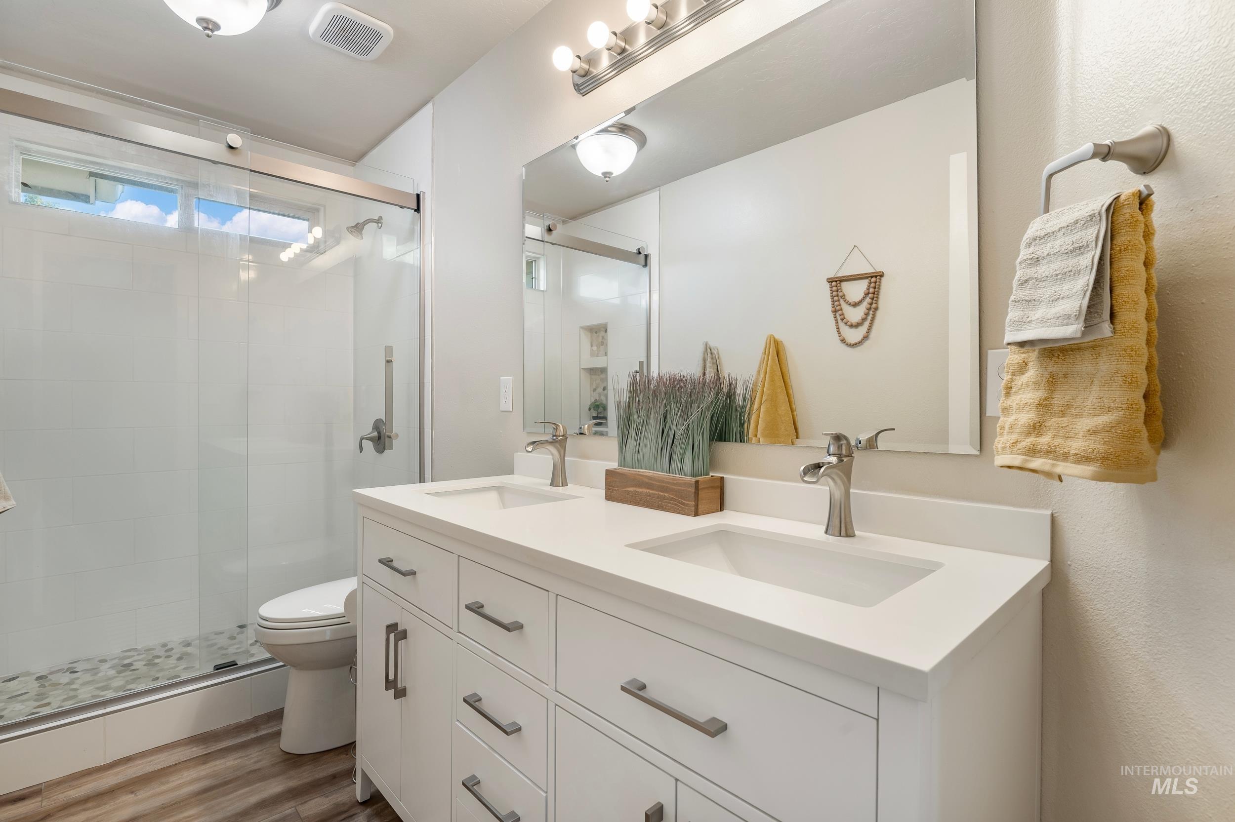 Bathroom featuring a stall shower, double vanity, and light wood-style flooring