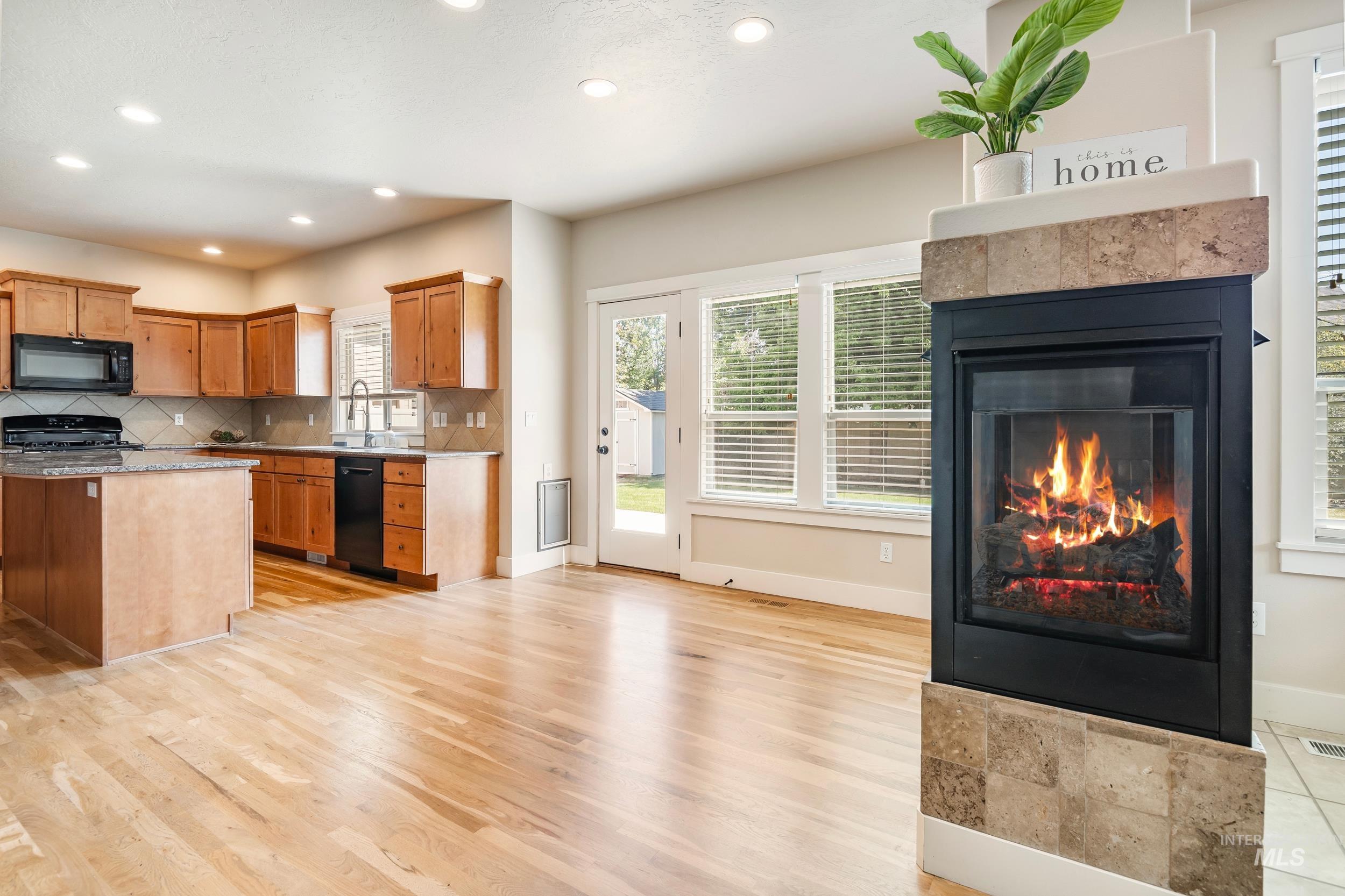 Kitchen with decorative backsplash, a tiled fireplace, light stone countertops, black appliances, and recessed lighting