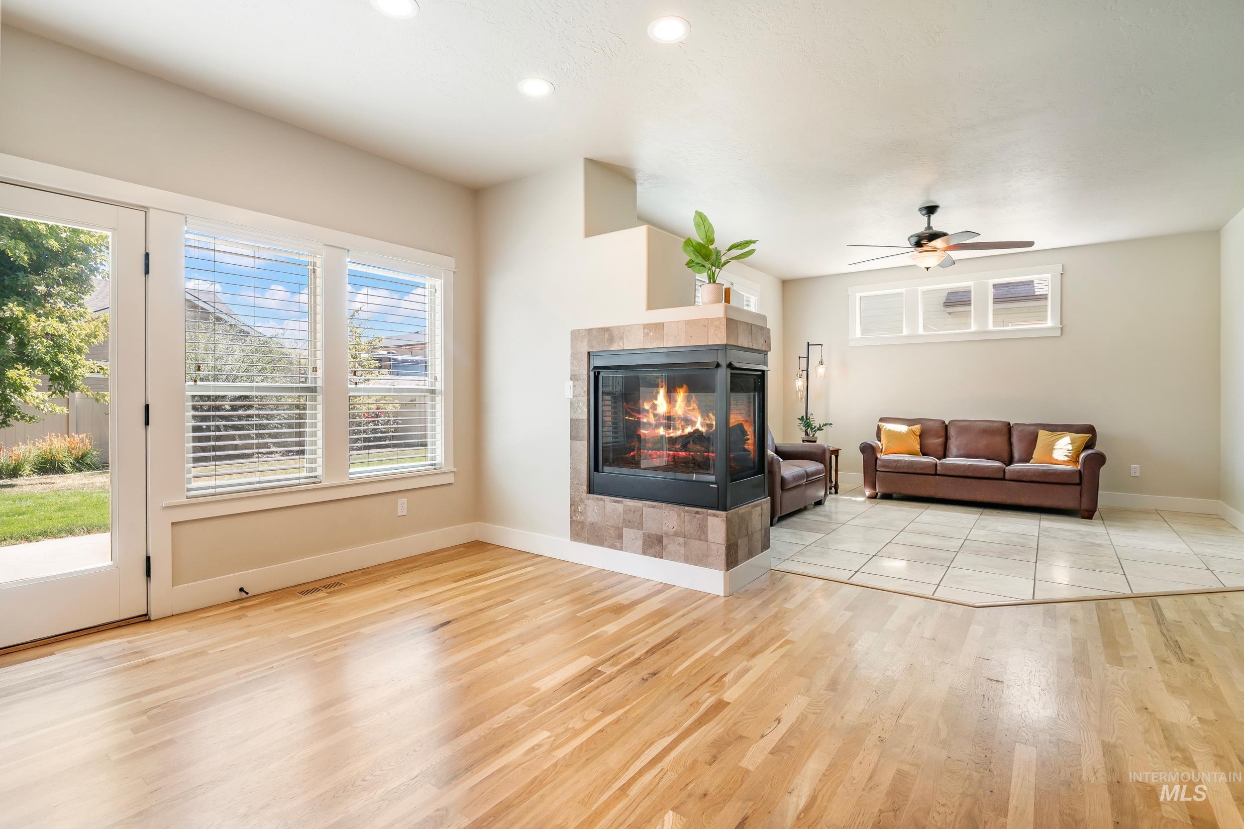Living area with ceiling fan, a tile fireplace, light wood finished floors, and recessed lighting