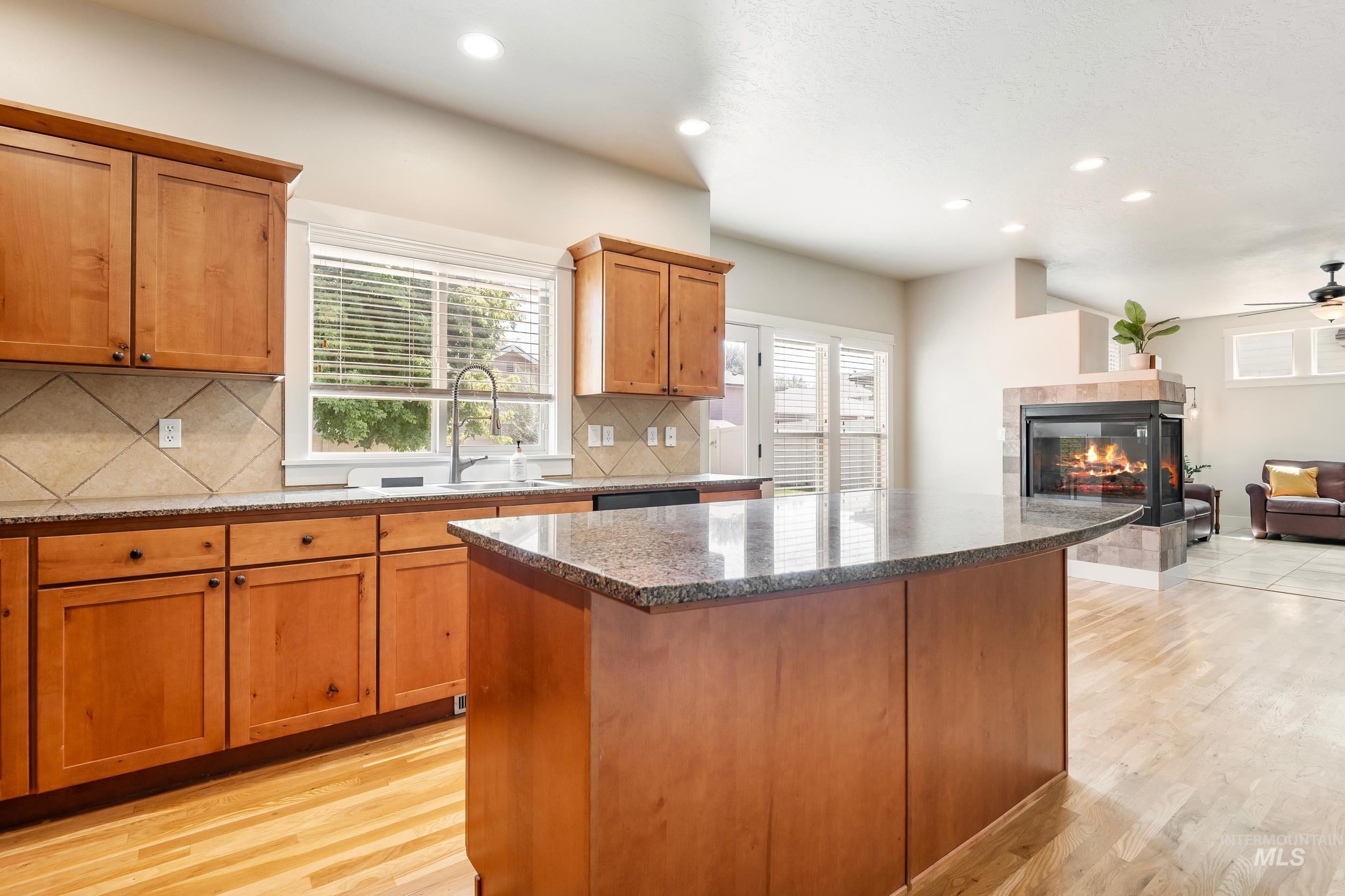 Kitchen featuring dark stone counters, open floor plan, recessed lighting, light wood-style flooring, and brown cabinets