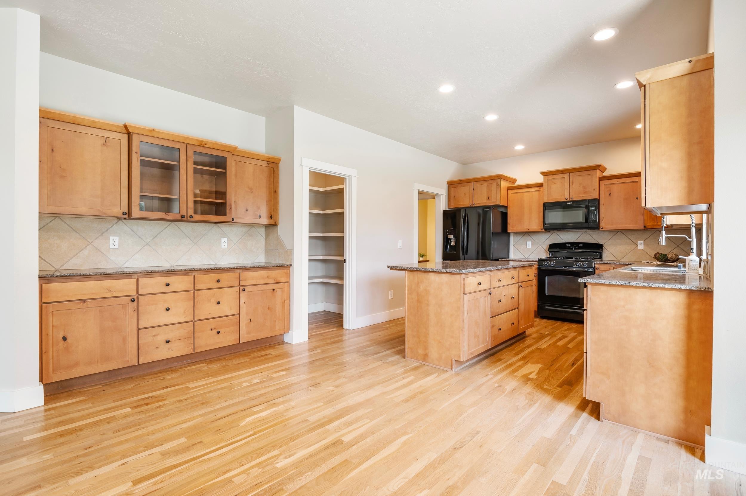 Kitchen with decorative backsplash, black appliances, recessed lighting, light wood-style flooring, and a kitchen island