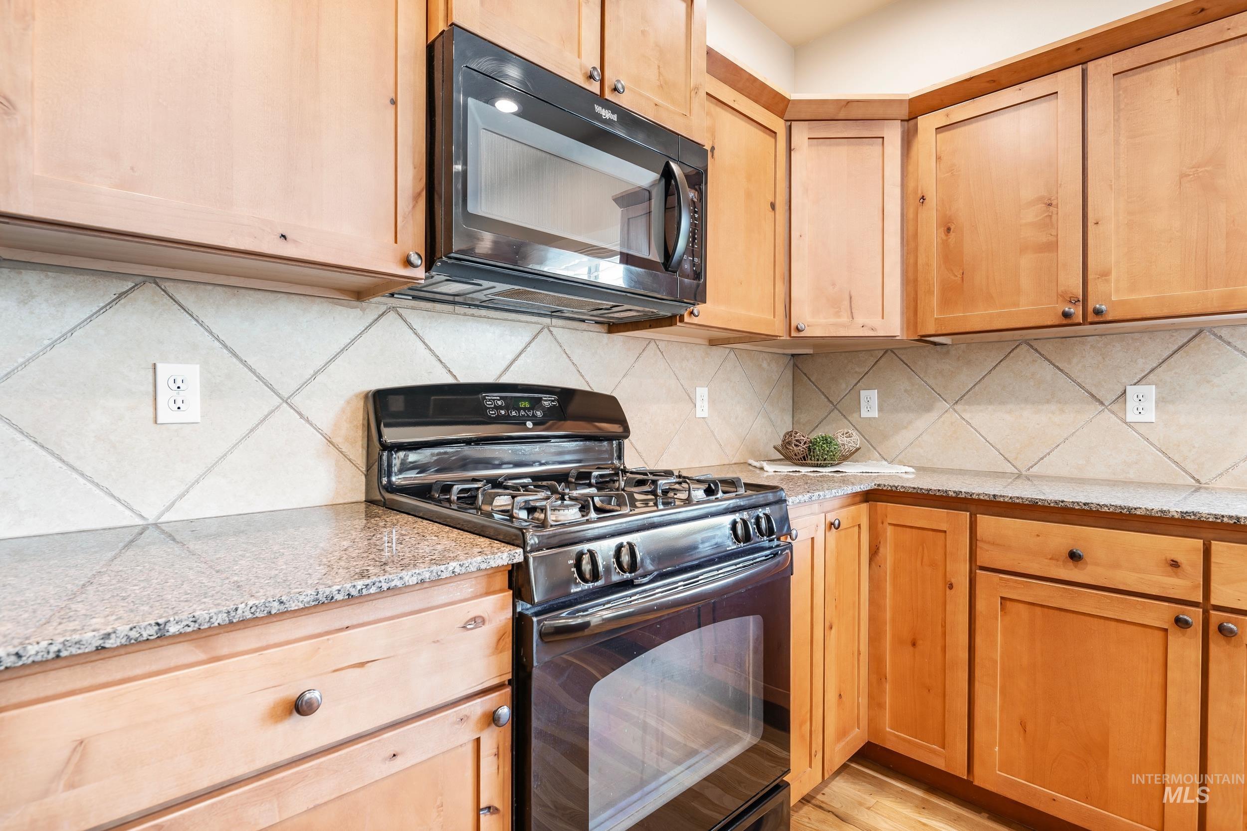 Kitchen featuring black appliances, light stone countertops, light brown cabinetry, backsplash, and light wood-type flooring
