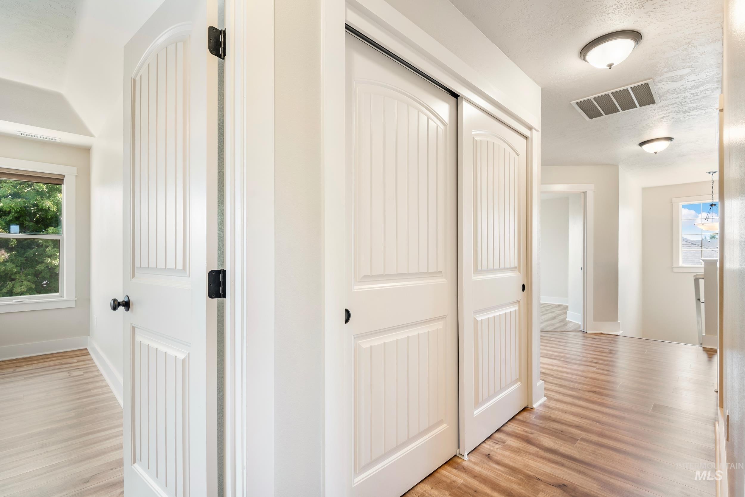 Corridor with healthy amount of natural light, light wood finished floors, and a textured ceiling