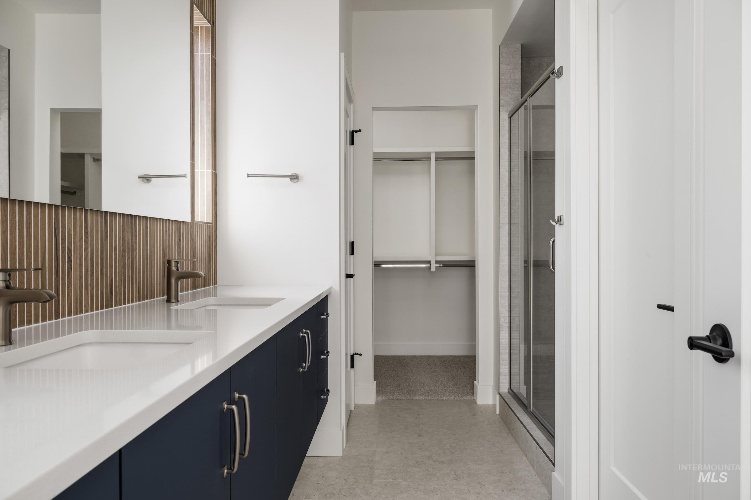Bathroom with a shower stall, double vanity, a spacious closet, and tile patterned floors
