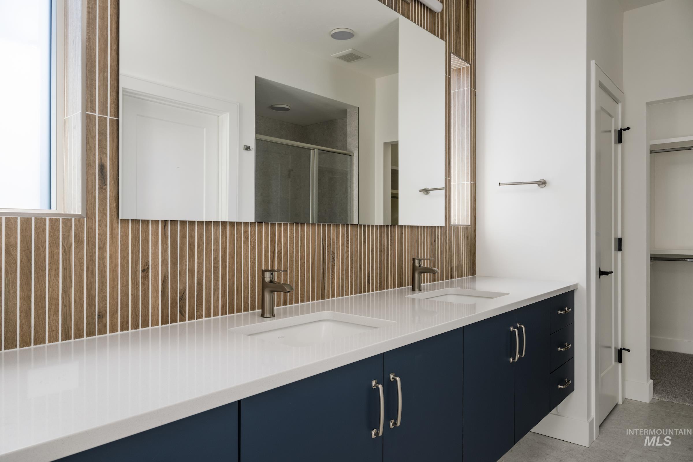 Full bath featuring a stall shower, double vanity, decorative backsplash, and a spacious closet