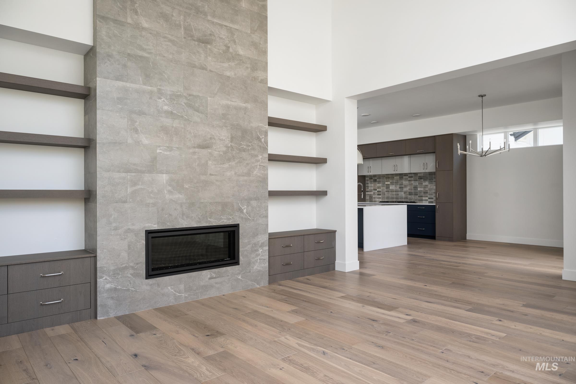 Unfurnished living room featuring a tiled fireplace, wood finished floors, and a chandelier