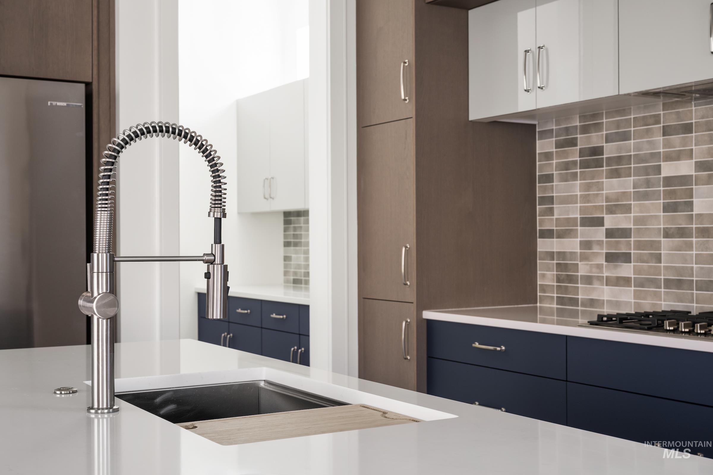 Kitchen with modern cabinets, decorative backsplash, light countertops, and stainless steel fridge