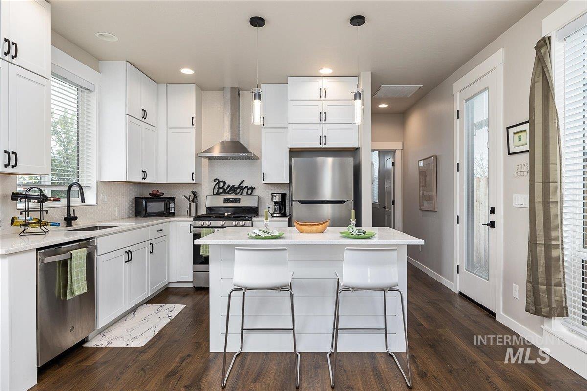 Kitchen featuring pendant lighting, stainless steel appliances, white cabinetry, a center island, and light stone countertops