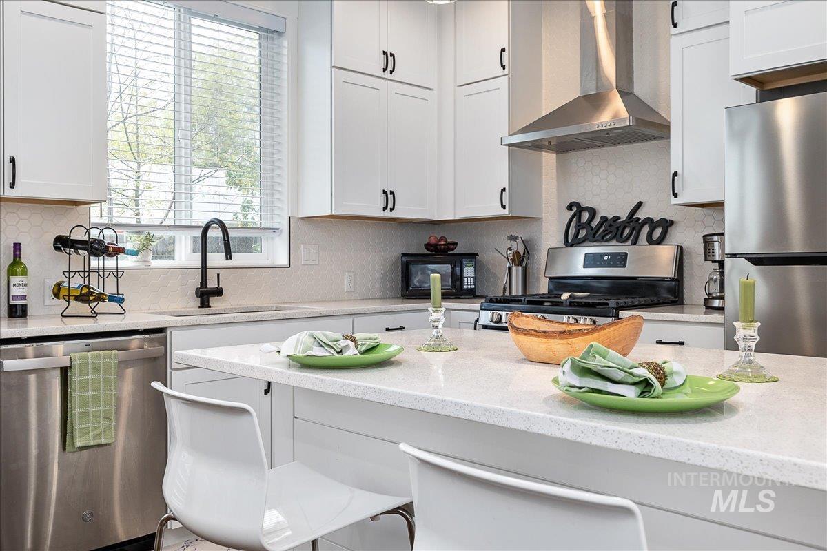 Kitchen with stainless steel appliances, light stone counters, a breakfast bar, backsplash, and white cabinetry