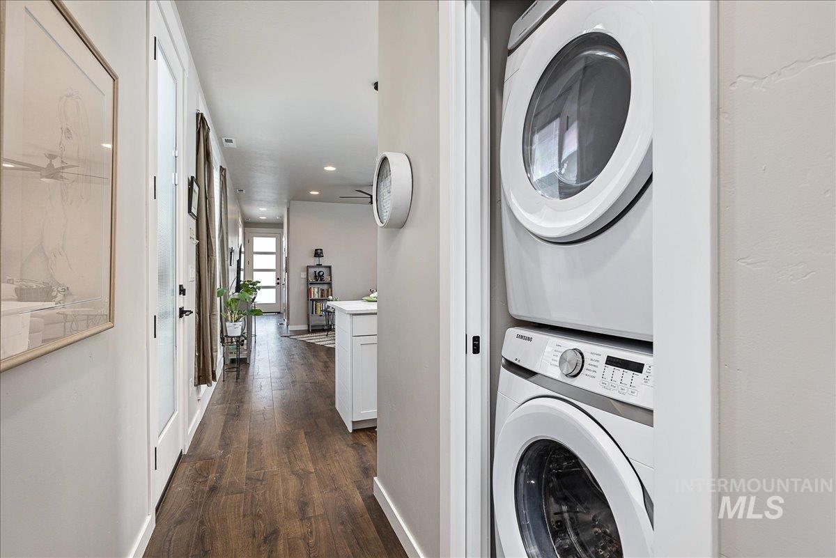 Laundry area featuring dark wood-type flooring, stacked washer and dryer, and recessed lighting