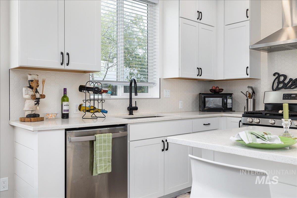 Kitchen with stainless steel appliances, white cabinets, light stone counters, and decorative backsplash