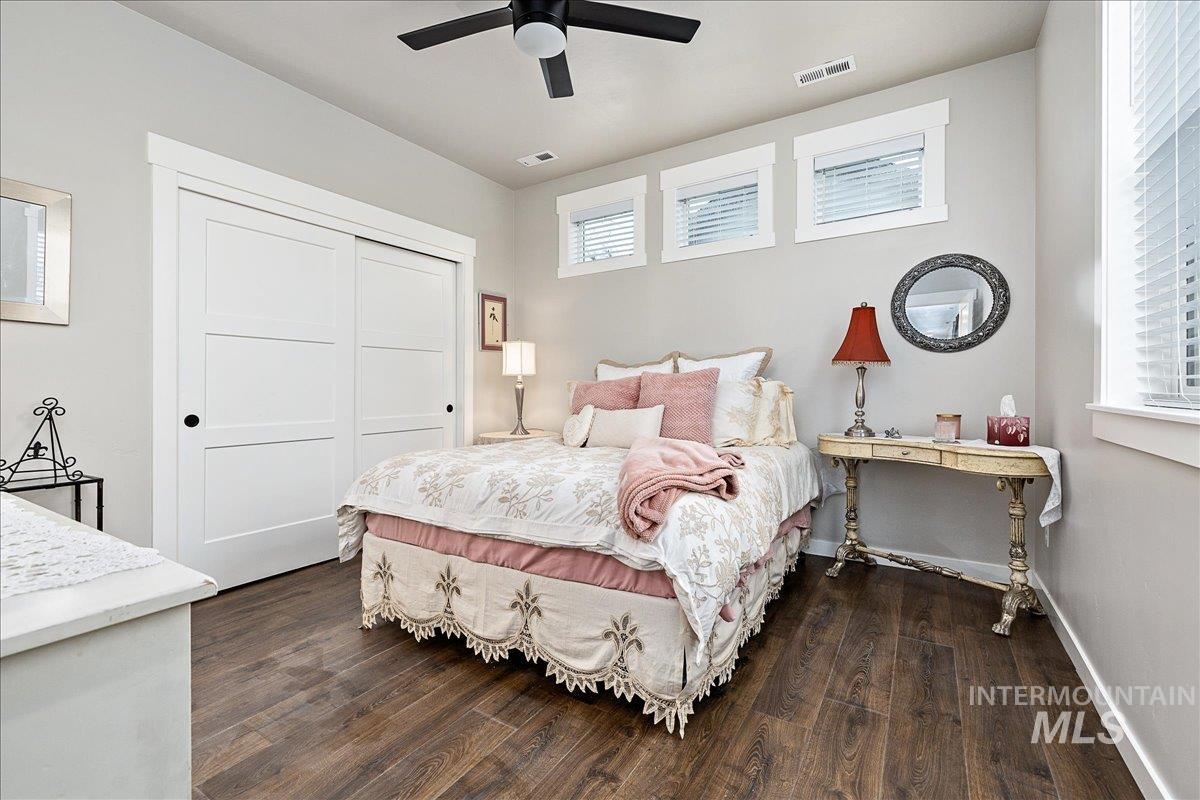 Bedroom with dark wood-style flooring, multiple windows, a ceiling fan, and a closet