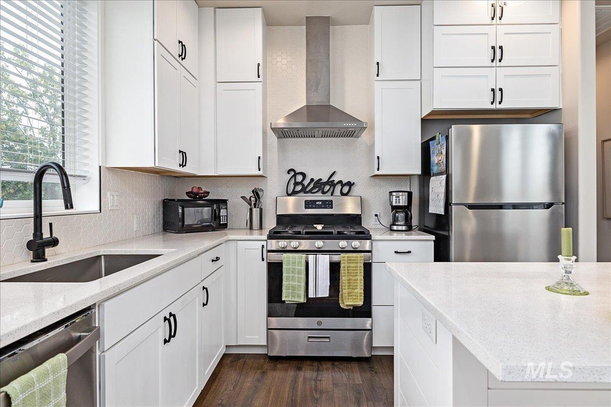 Kitchen with stainless steel appliances, white cabinets, dark wood-type flooring, and light stone counters