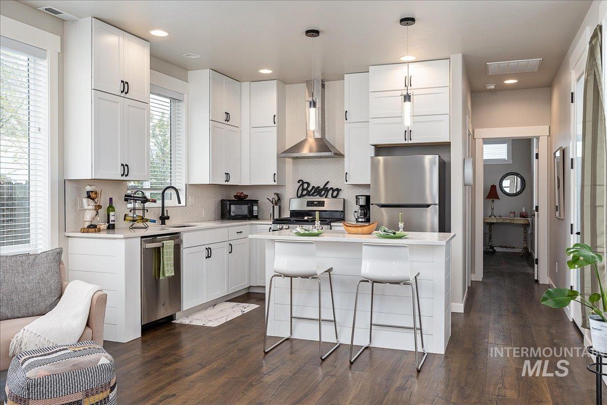 Kitchen featuring decorative light fixtures, stainless steel appliances, a kitchen island, and white cabinetry
