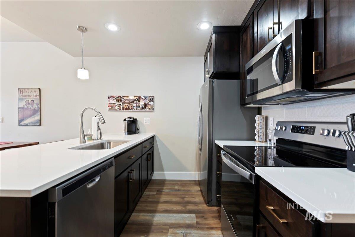 Kitchen with stainless steel appliances, a peninsula, dark wood finished floors, dark wood finish cabinets, and pendant lighting
