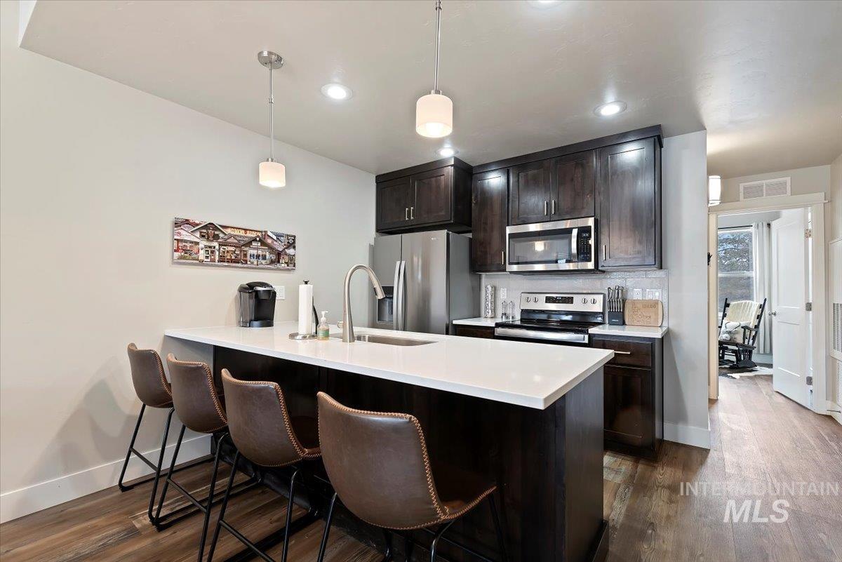 Kitchen featuring a peninsula, a kitchen breakfast bar, stainless steel appliances, decorative light fixtures, and dark wood finish cabinets