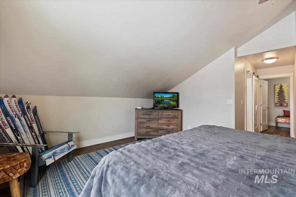 Bedroom with a barn door, vaulted ceiling, and dark wood finished floors