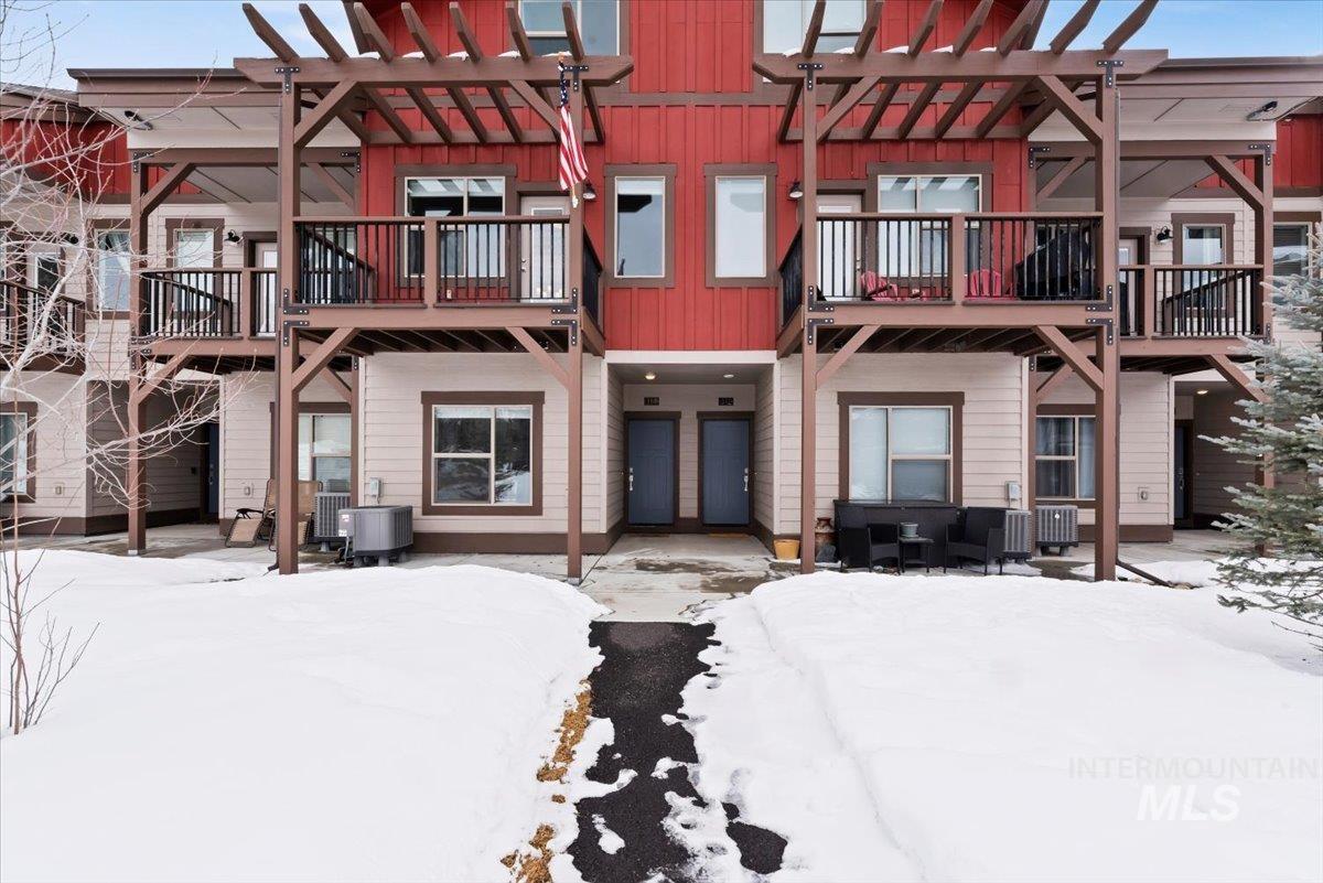 Snow covered back of property with a patio, board and batten siding, and a pergola
