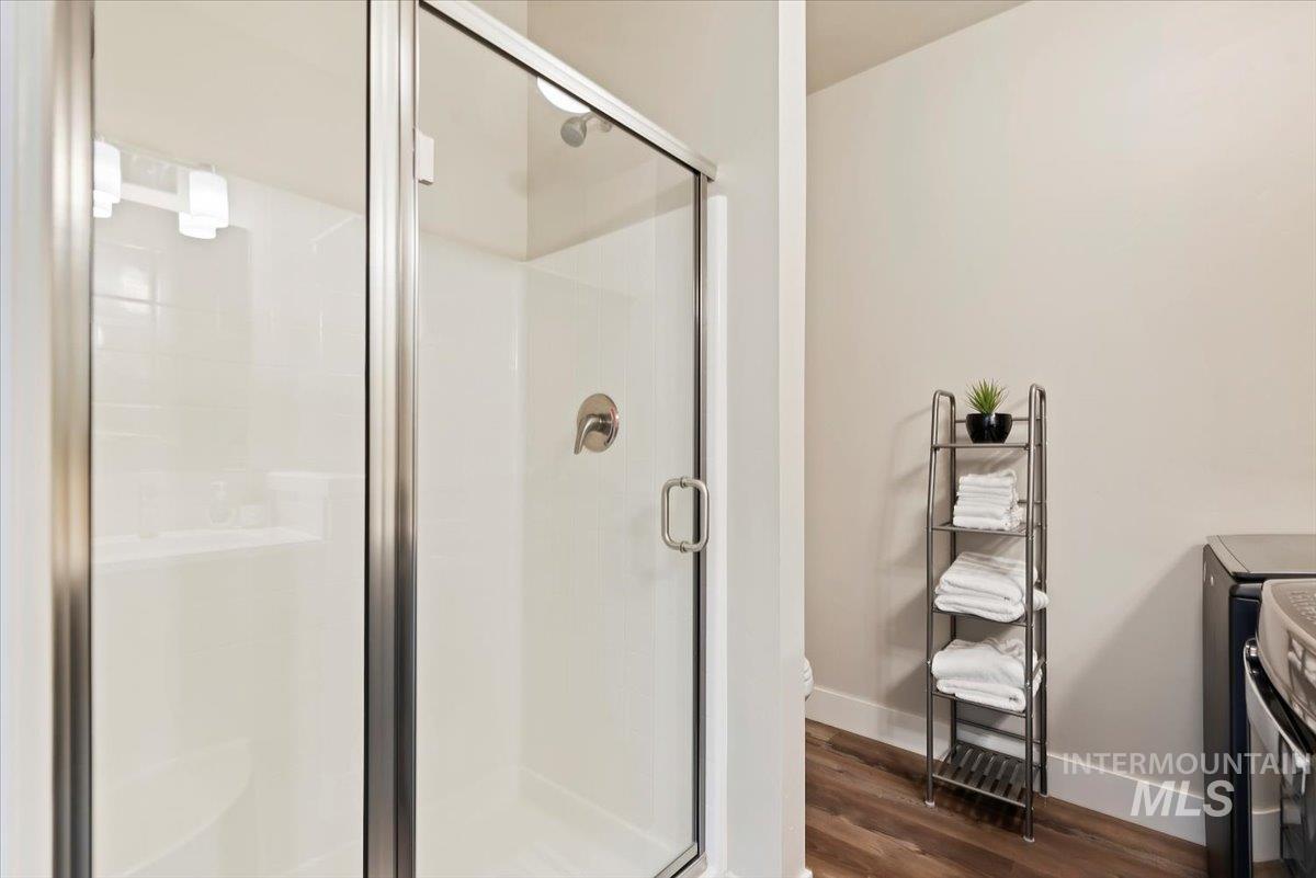 Bathroom with a shower stall, dark wood-style flooring, and washer and clothes dryer