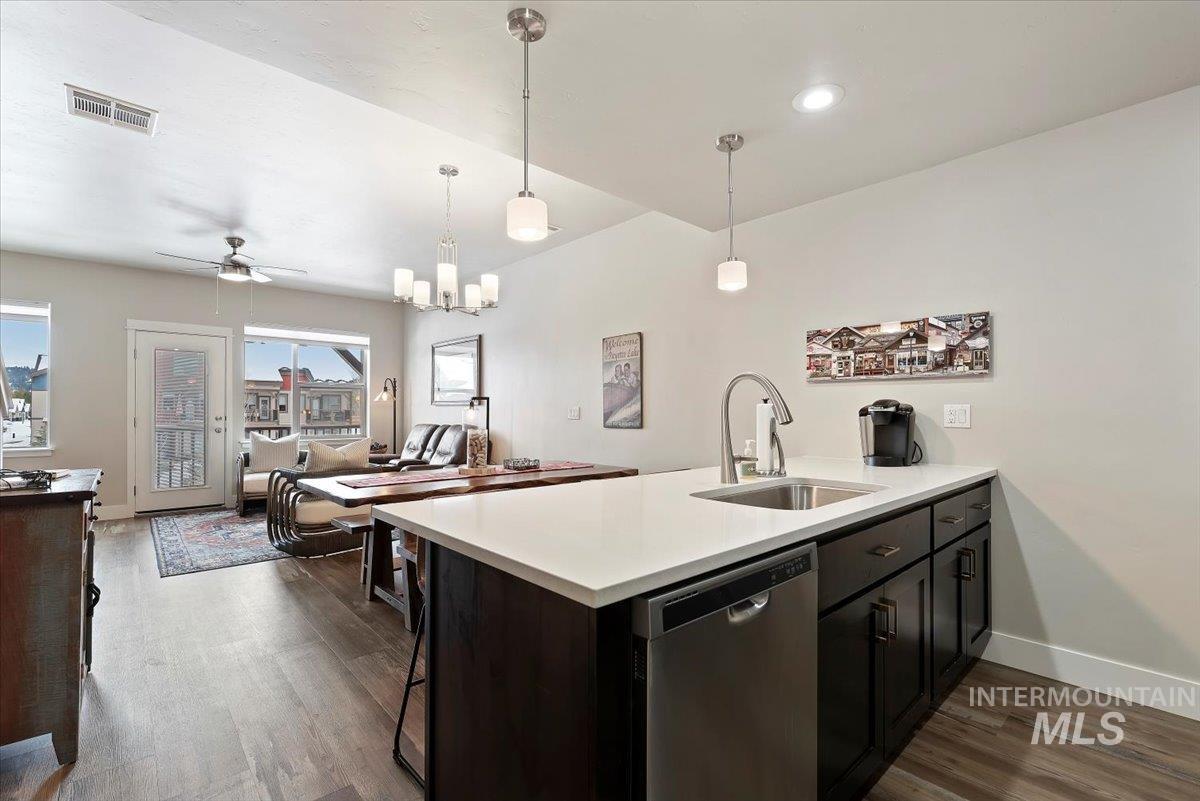 Kitchen featuring a peninsula, stainless steel dishwasher, open floor plan, dark wood-style floors, and suspended lighting