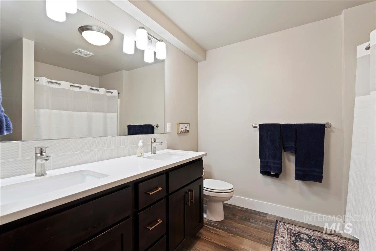 Full bathroom with double vanity, a shower with shower curtain, and dark wood finished floors