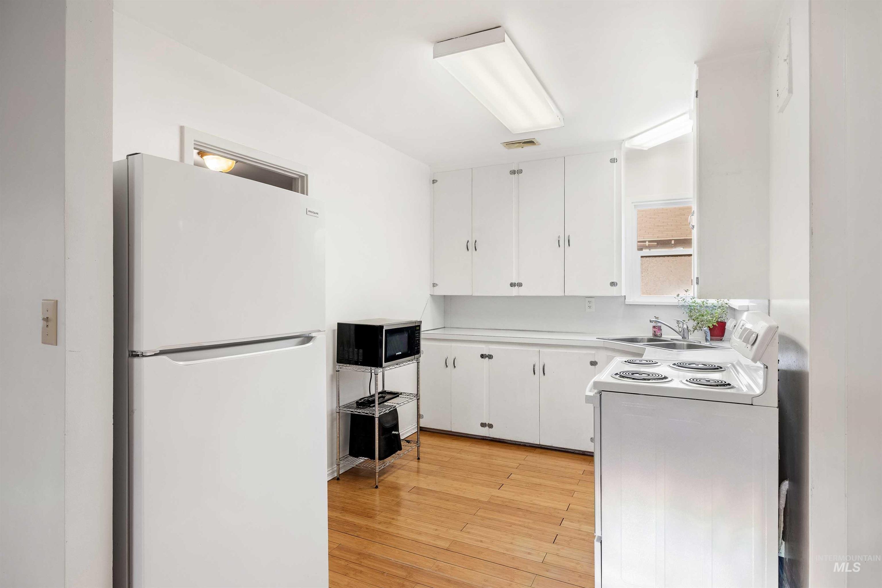 Kitchen with white appliances, light countertops, white cabinets, and light wood-style flooring
