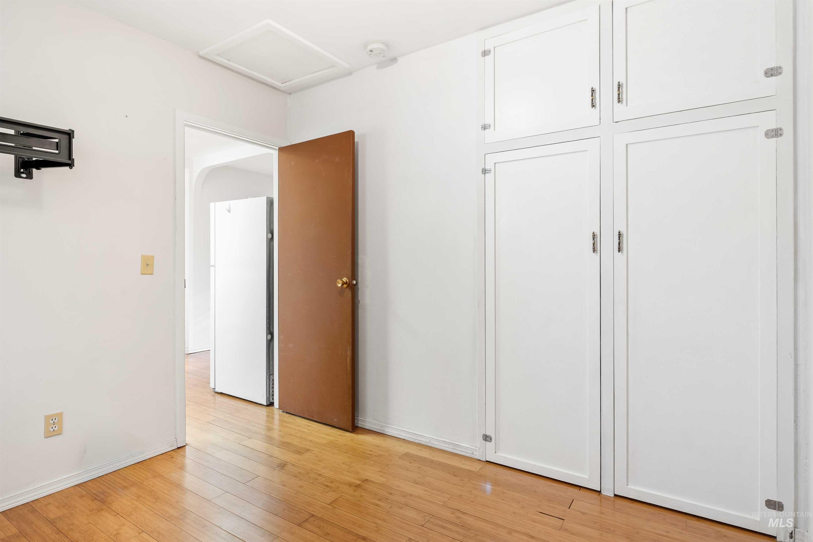Unfurnished bedroom featuring attic access, light wood-type flooring, and freestanding refrigerator