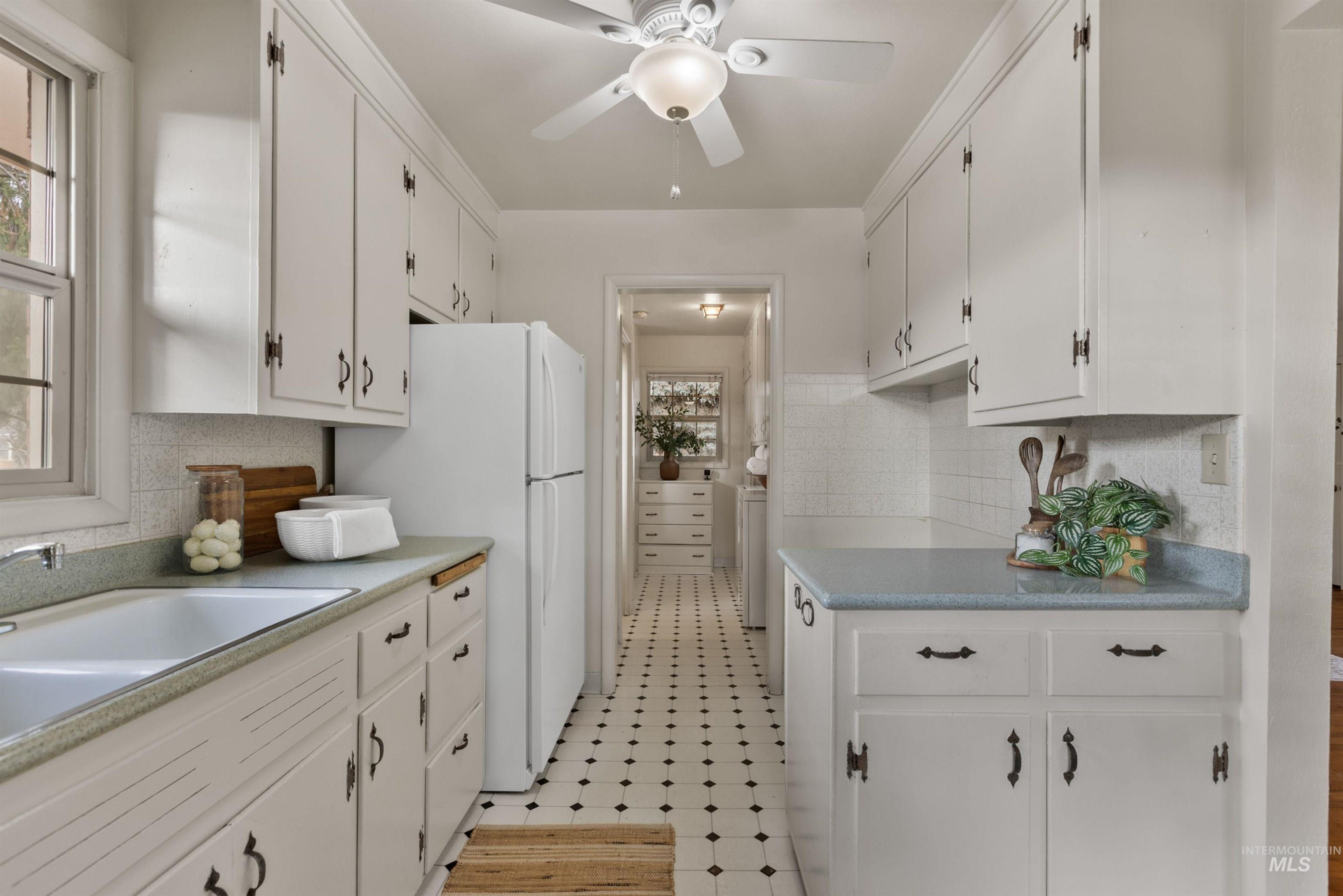 Kitchen featuring light countertops, white cabinetry, freestanding refrigerator, and decorative backsplash