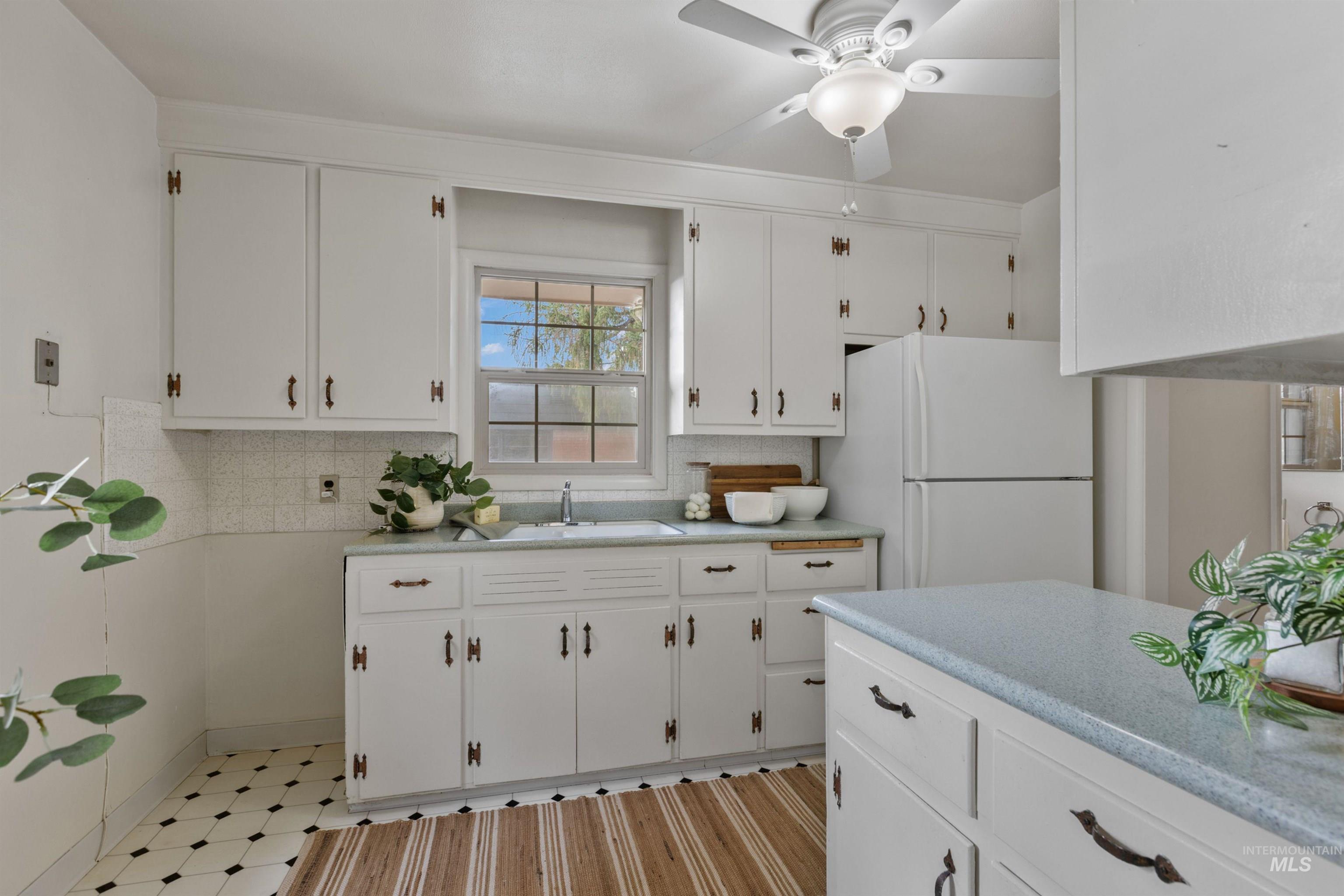 Kitchen featuring white cabinetry, freestanding refrigerator, light floors, a ceiling fan, and tasteful backsplash