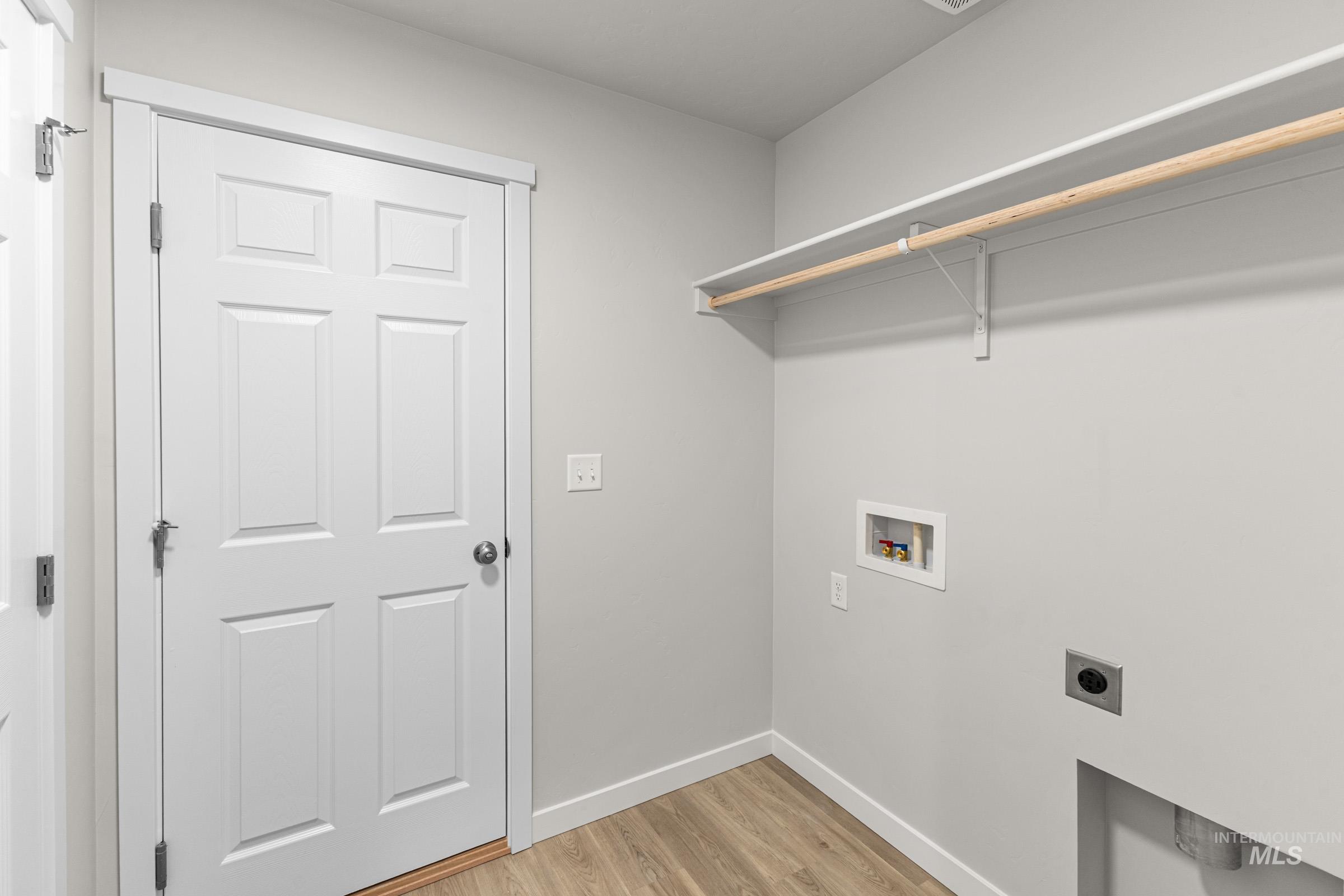 Dedicated laundry area featuring a multi-panel door, wood-finish flooring, a built-in shelf with hanging rod, and utility hookups