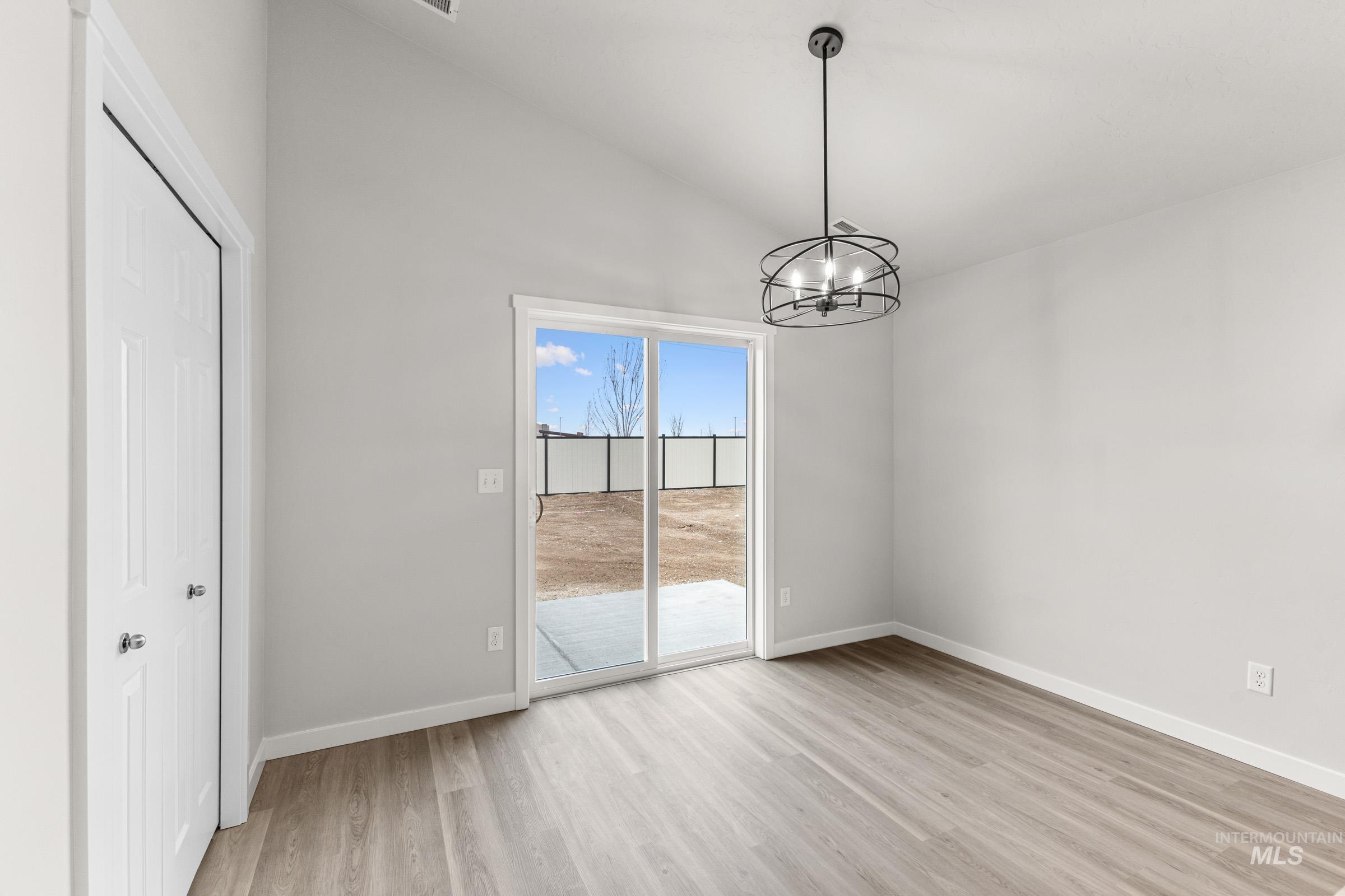 Vaulted ceiling interior space featuring wood-finish flooring, a modern chandelier, and sliding glass doors opening to a concrete patio