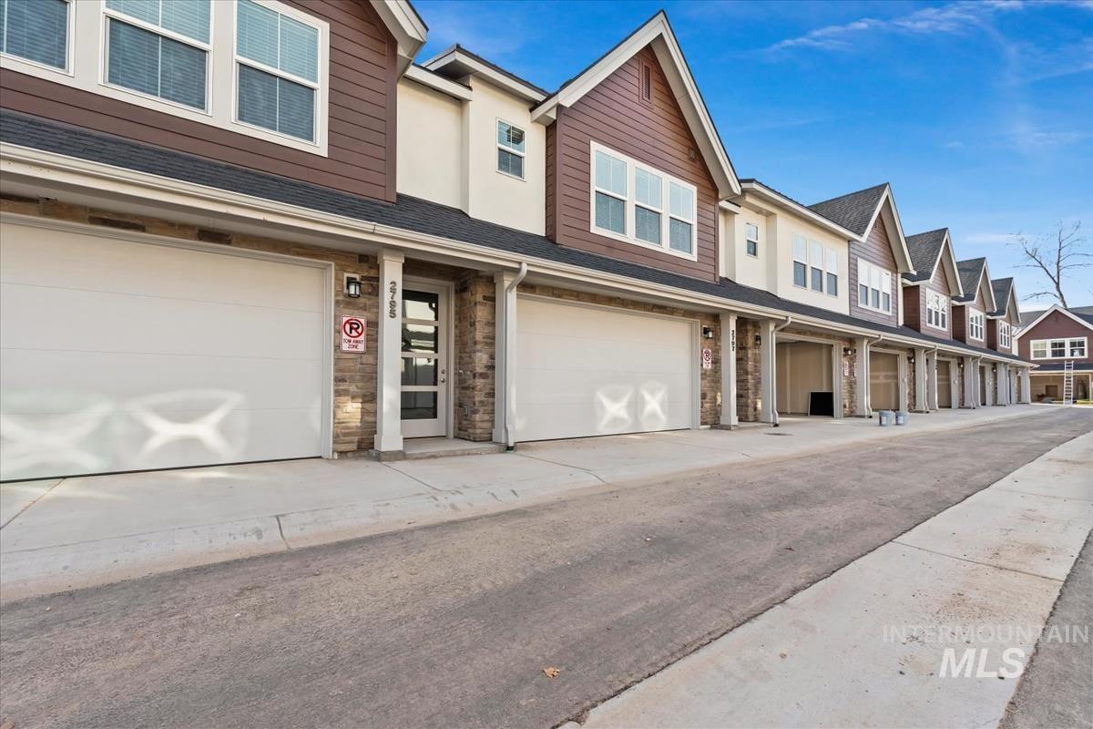 Traditional-style home featuring stone siding, a residential view, roof with shingles, and an attached garage