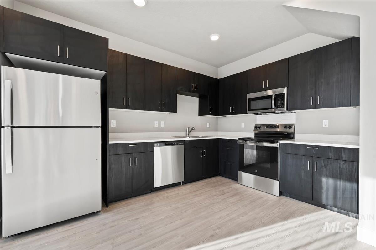 Kitchen with appliances with stainless steel finishes, light countertops, light wood-type flooring, and dark cabinetry