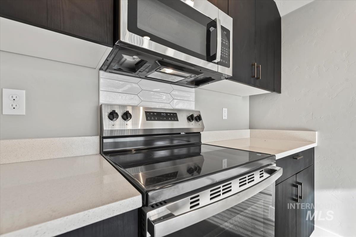 Kitchen with appliances with stainless steel finishes, a textured wall, modern cabinets, light stone countertops, and tasteful backsplash