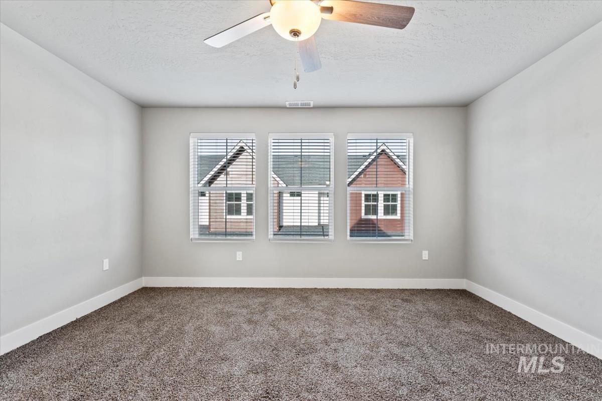 Carpeted empty room with a textured ceiling and ceiling fan