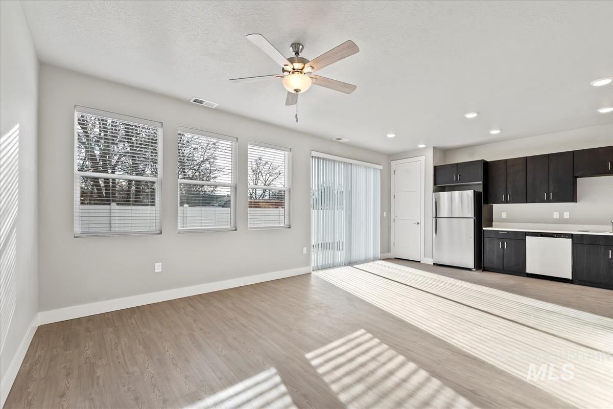 Kitchen with freestanding refrigerator, white dishwasher, dark cabinets, light countertops, and a ceiling fan