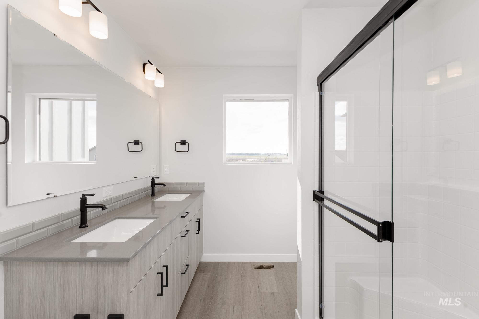 Bathroom with double vanity, a stall shower, and light wood-type flooring