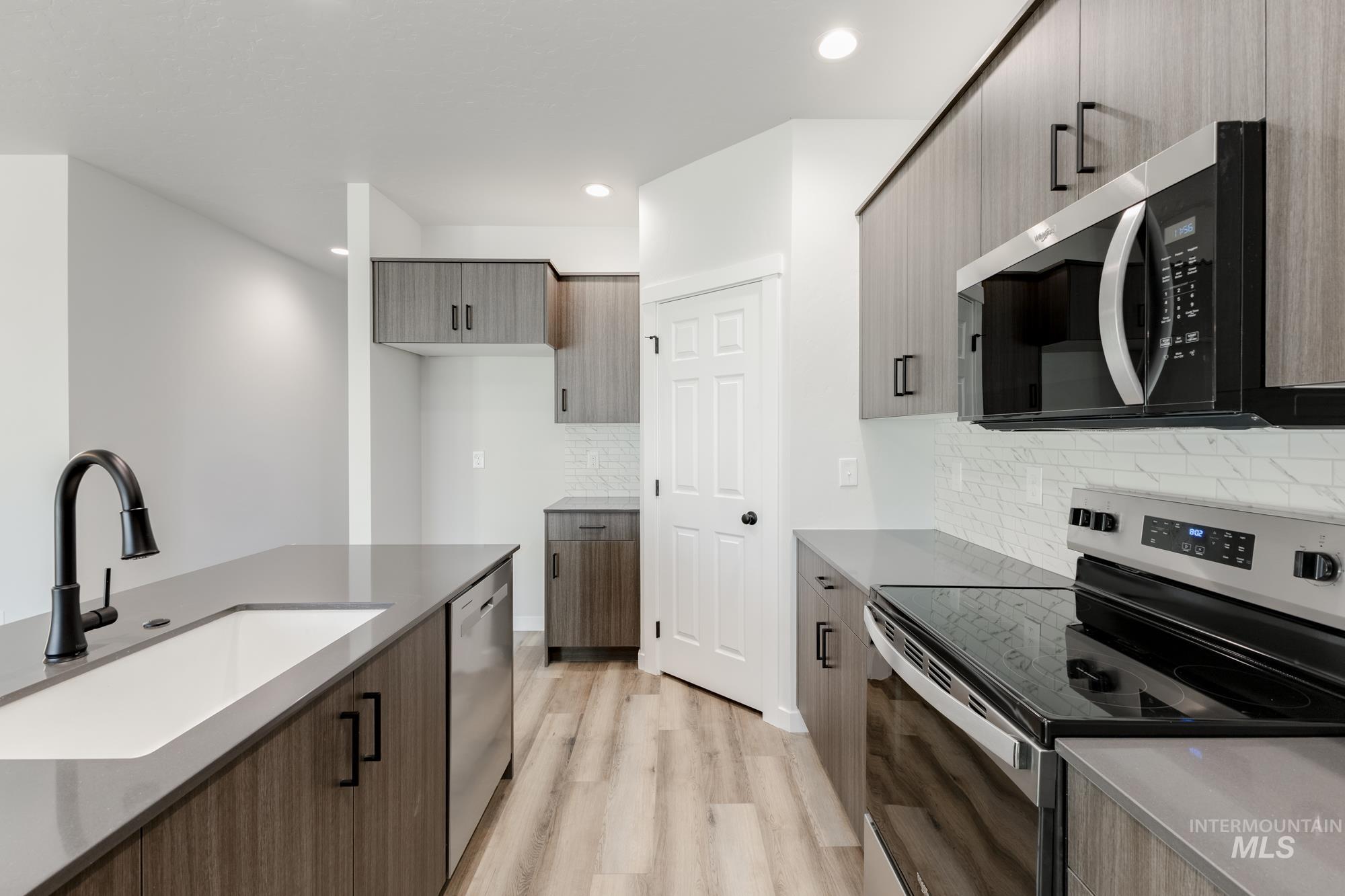 Kitchen featuring stainless steel appliances, modern cabinets, light stone countertops, recessed lighting, and light wood-style flooring
