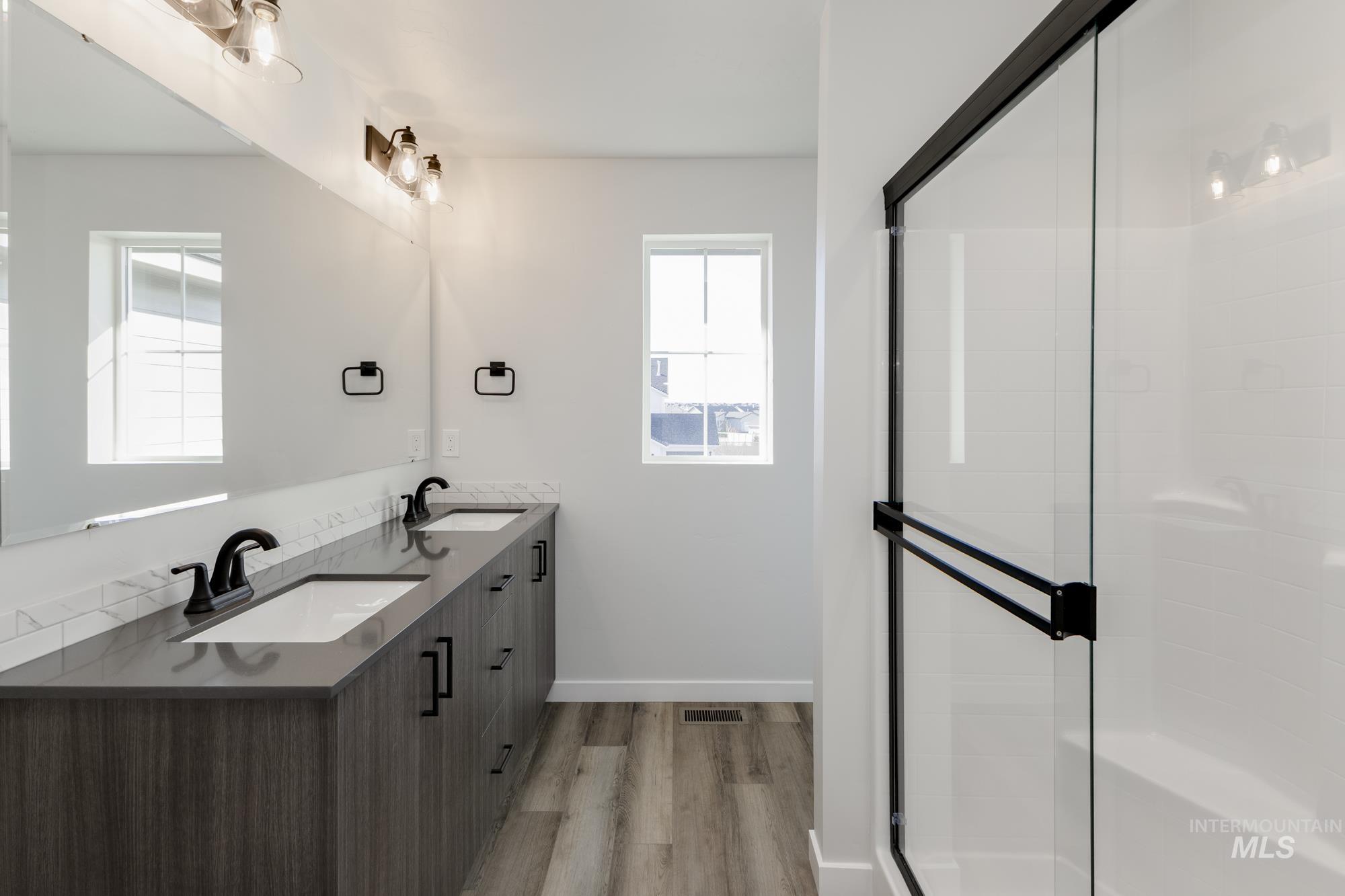 Full bathroom featuring double vanity, a shower stall, and light wood-style flooring