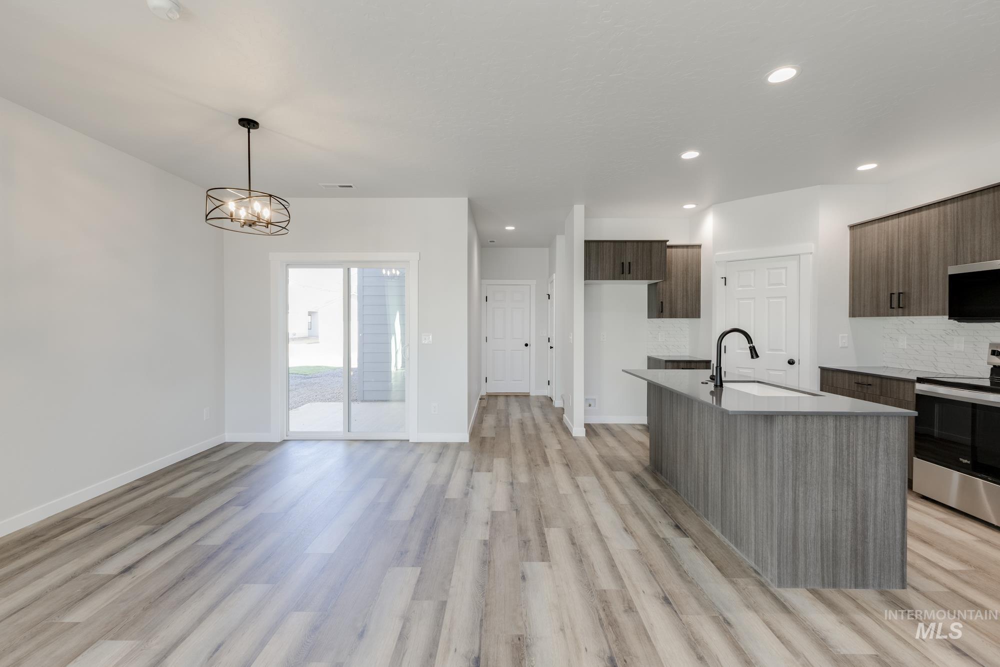 Kitchen featuring electric range, modern cabinets, a center island with sink, light wood-style floors, and dark brown cabinets