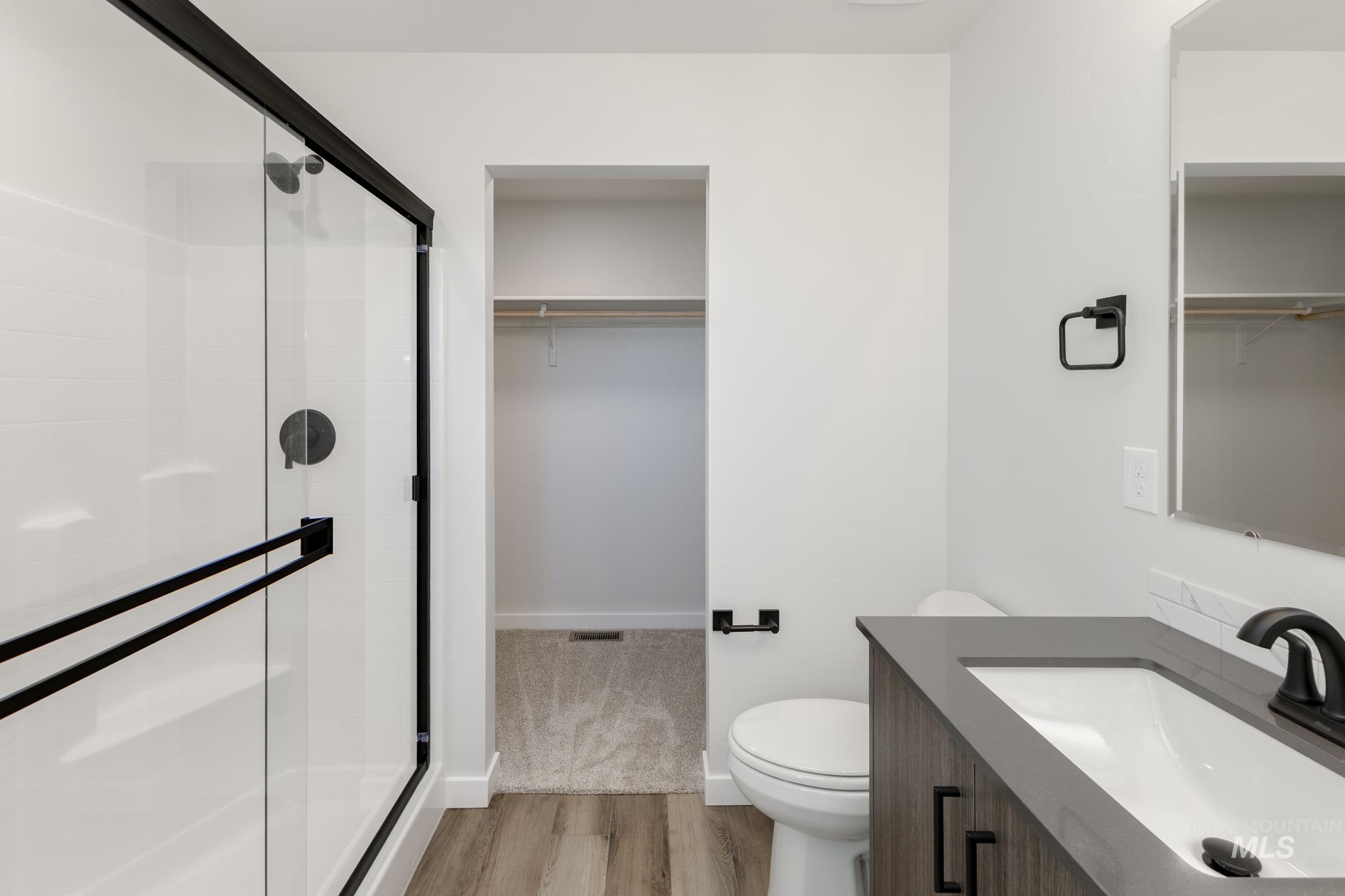 Full bath with a walk in closet, vanity, a stall shower, and light wood-style flooring