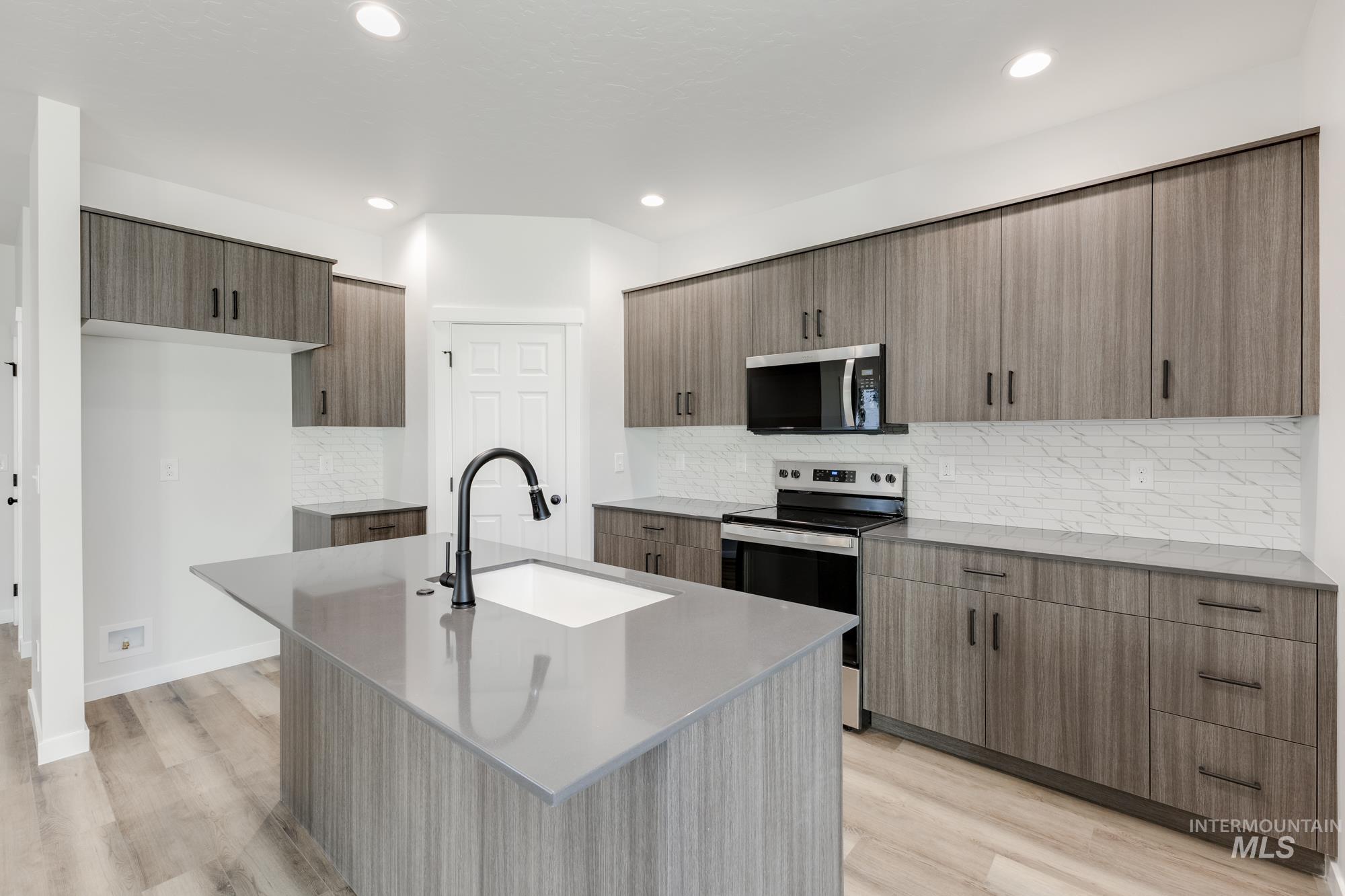 Kitchen featuring appliances with stainless steel finishes, an island with sink, light stone countertops, tasteful backsplash, and recessed lighting
