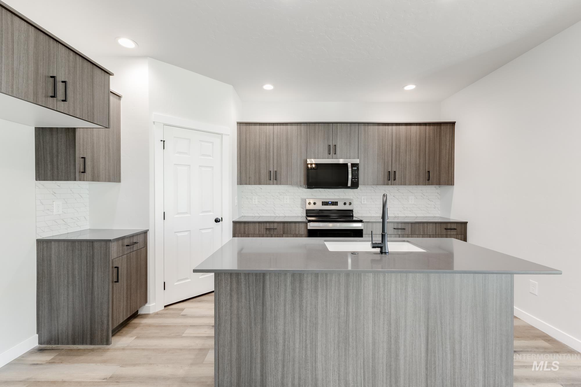Kitchen with tasteful backsplash, modern cabinets, stainless steel appliances, light stone countertops, and a kitchen island with sink
